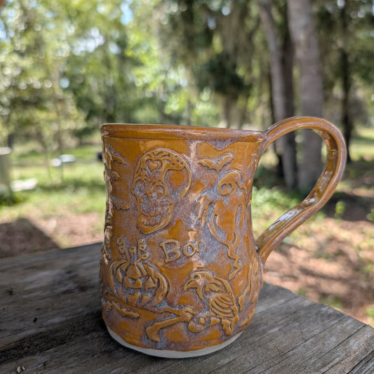 Yellowish-orange ceramic mug with embossed designs on a wooden surface outdoors