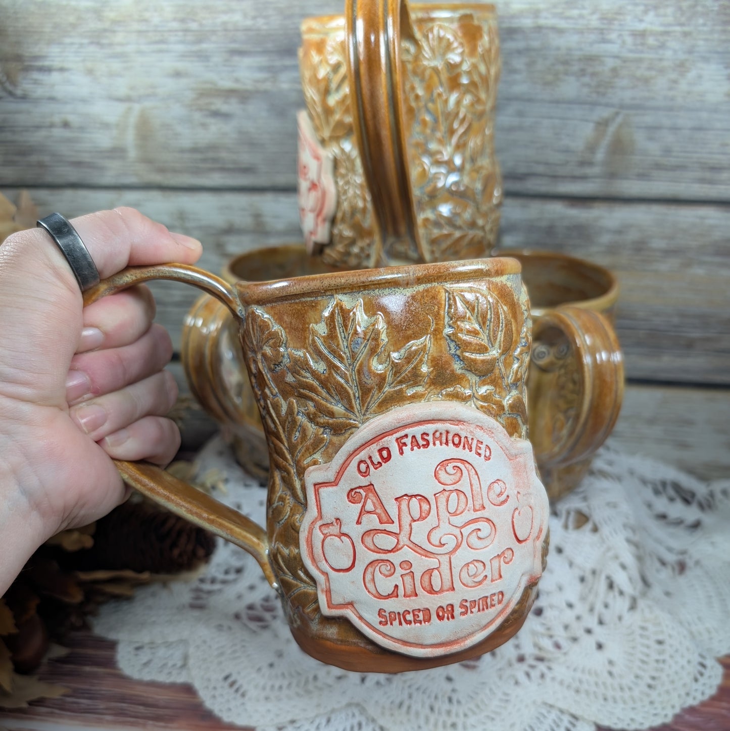 Ceramic mug with 'Old Fashioned Apple Cider' label held by a hand on a wooden surface.