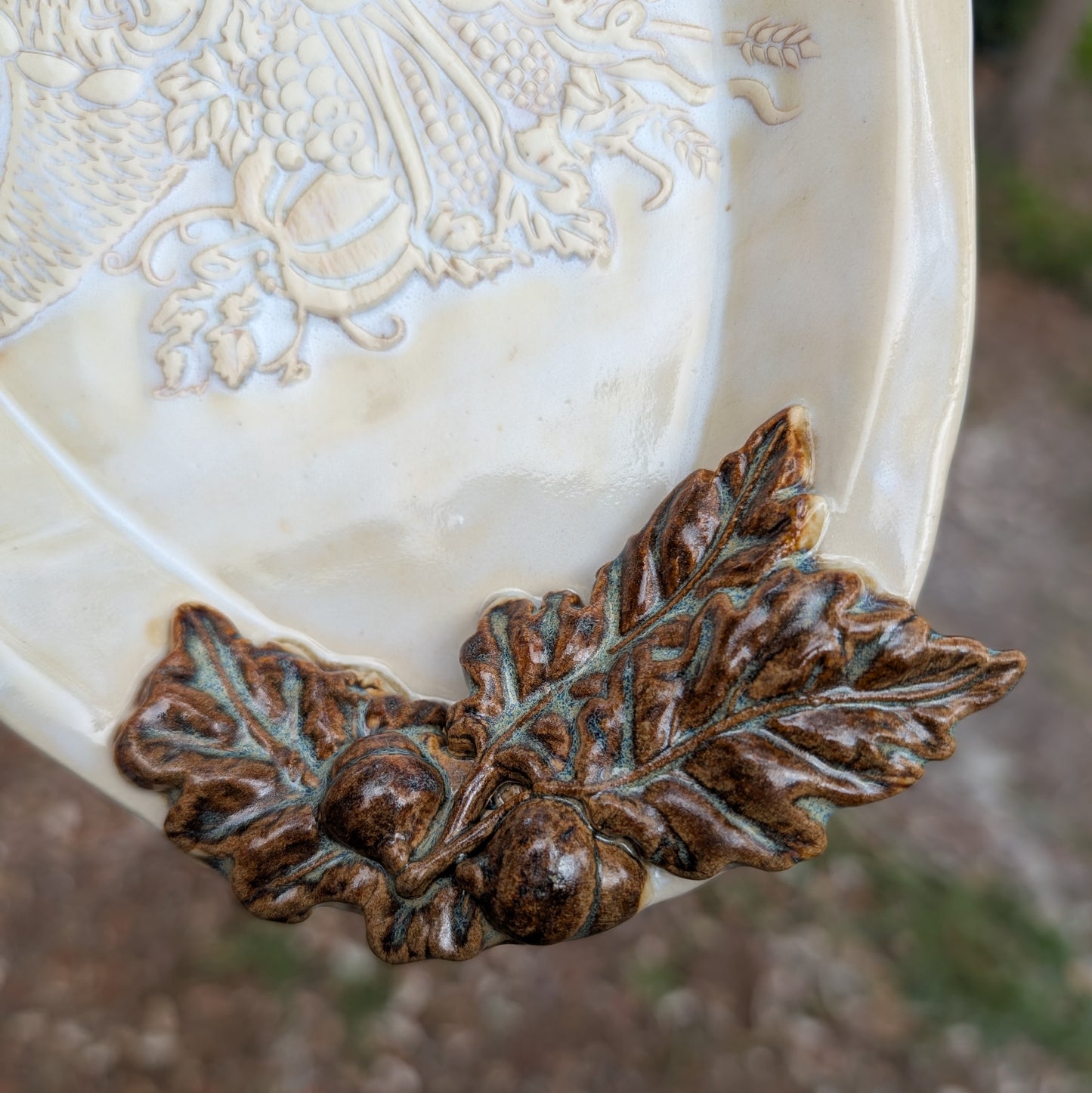 Decorative ceramic plate with leaf and acorn design on a blurred natural background