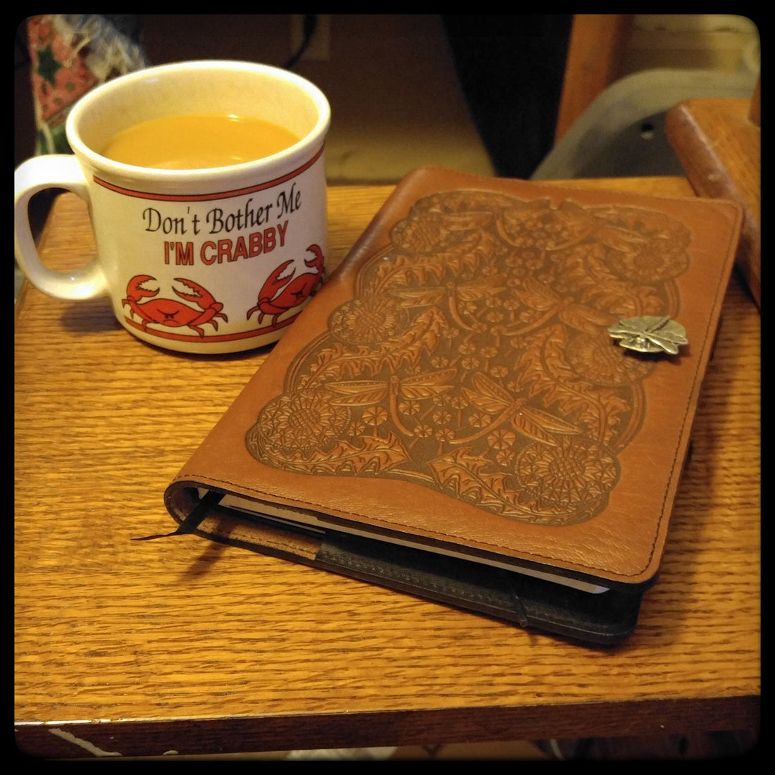 A leather journal and a coffee mug on a wooden desk.