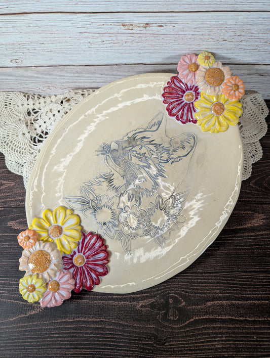 An oval tray decorated with a cat's face and flowers, with flowered handles, on a white lace doily on a wooden background.