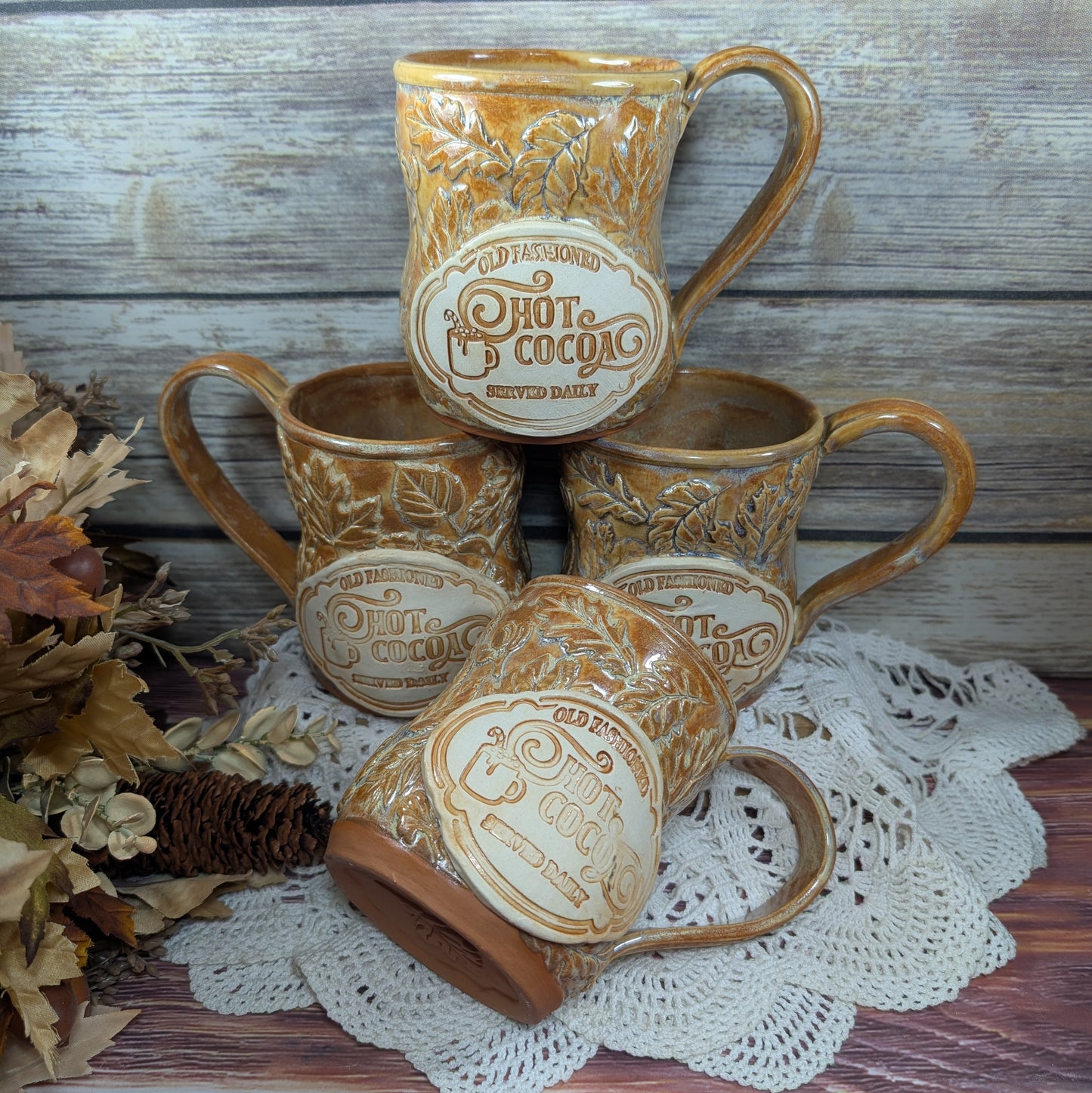 Set of four ceramic mugs with 'Hot Cocoa' text on a wooden surface with a doily.