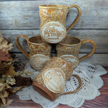 Set of four ceramic mugs with 'Hot Cocoa' text on a wooden surface with a doily.