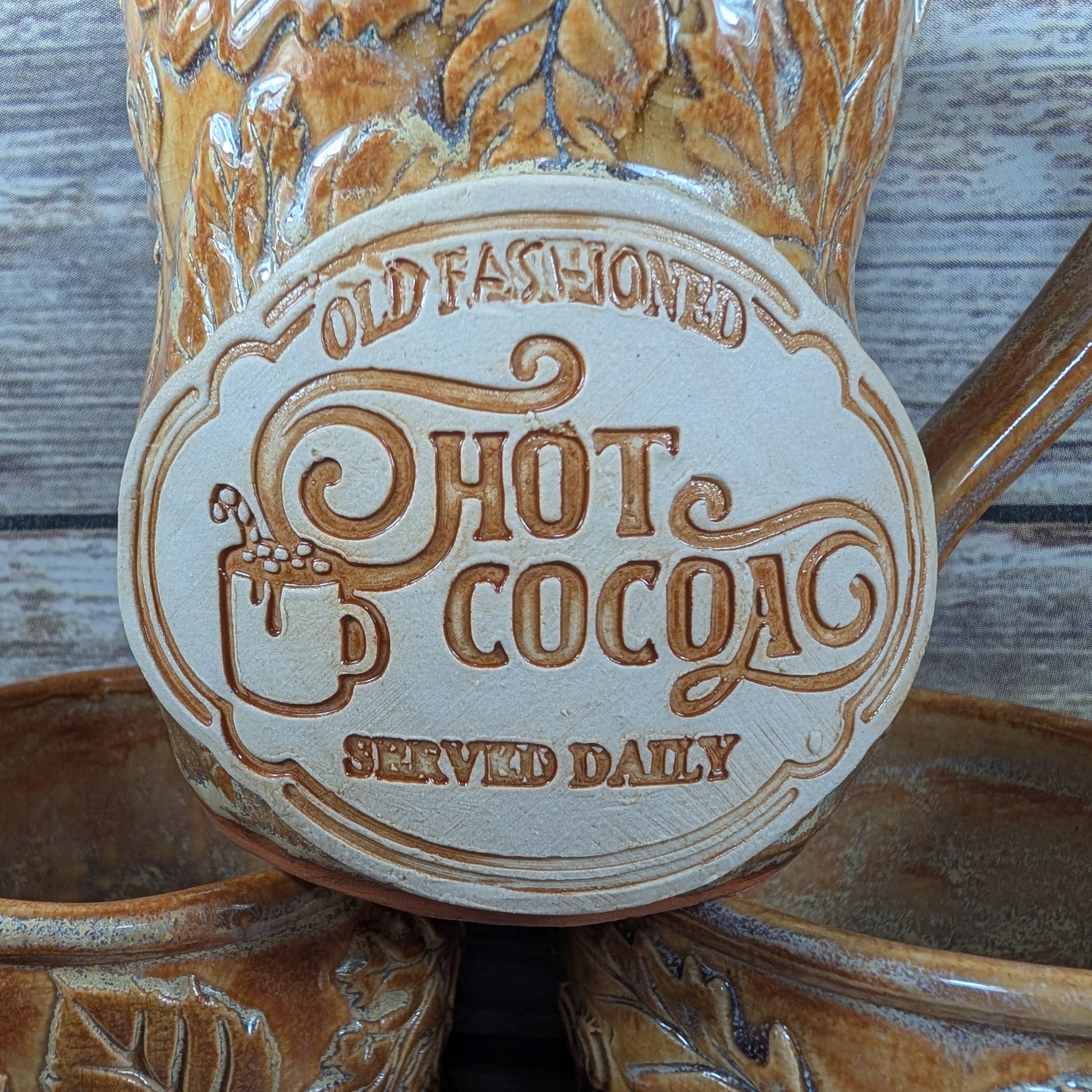 Ceramic mug with 'Old Fashioned Hot Cocoa Served Daily' text on a wooden surface
