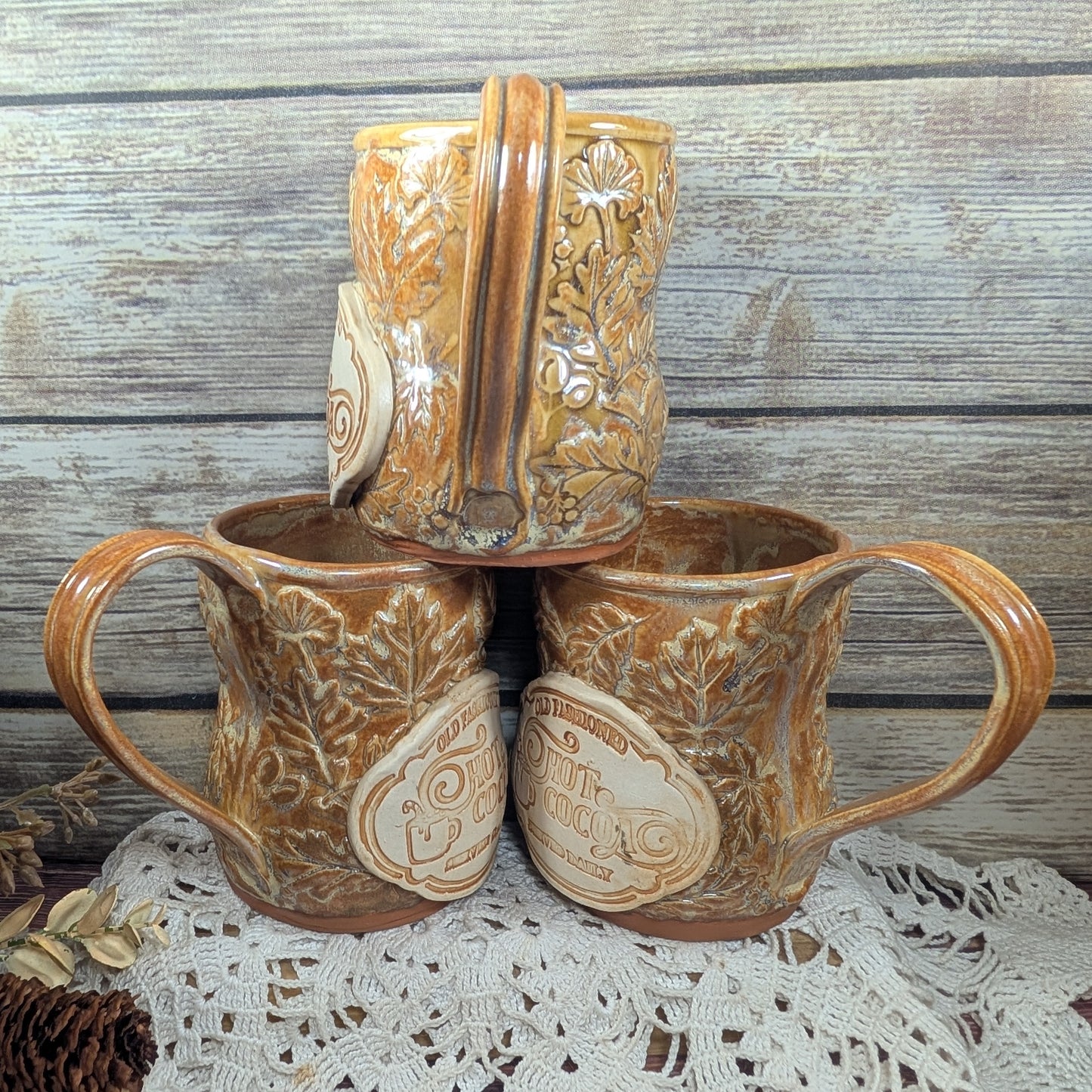 Three ceramic mugs with embossed designs on a lace tablecloth against a wooden background