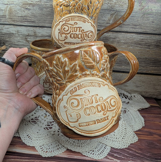 Ceramic hot cocoa mugs with 'Old Fashioned Hot Cocoa' branding on a wooden surface.