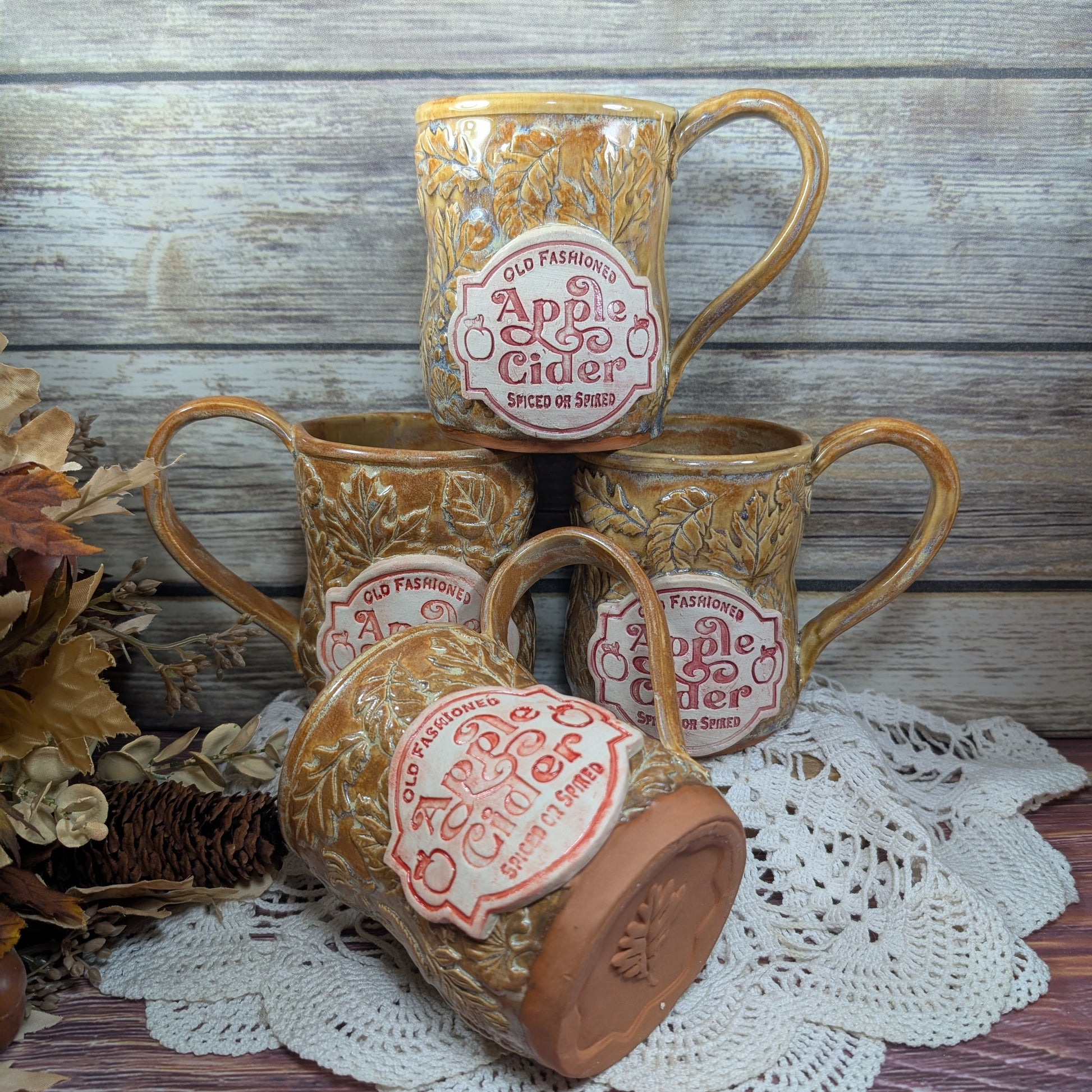 Set of four ceramic mugs with 'Old Fashioned Apple Cider' label on a wooden surface.