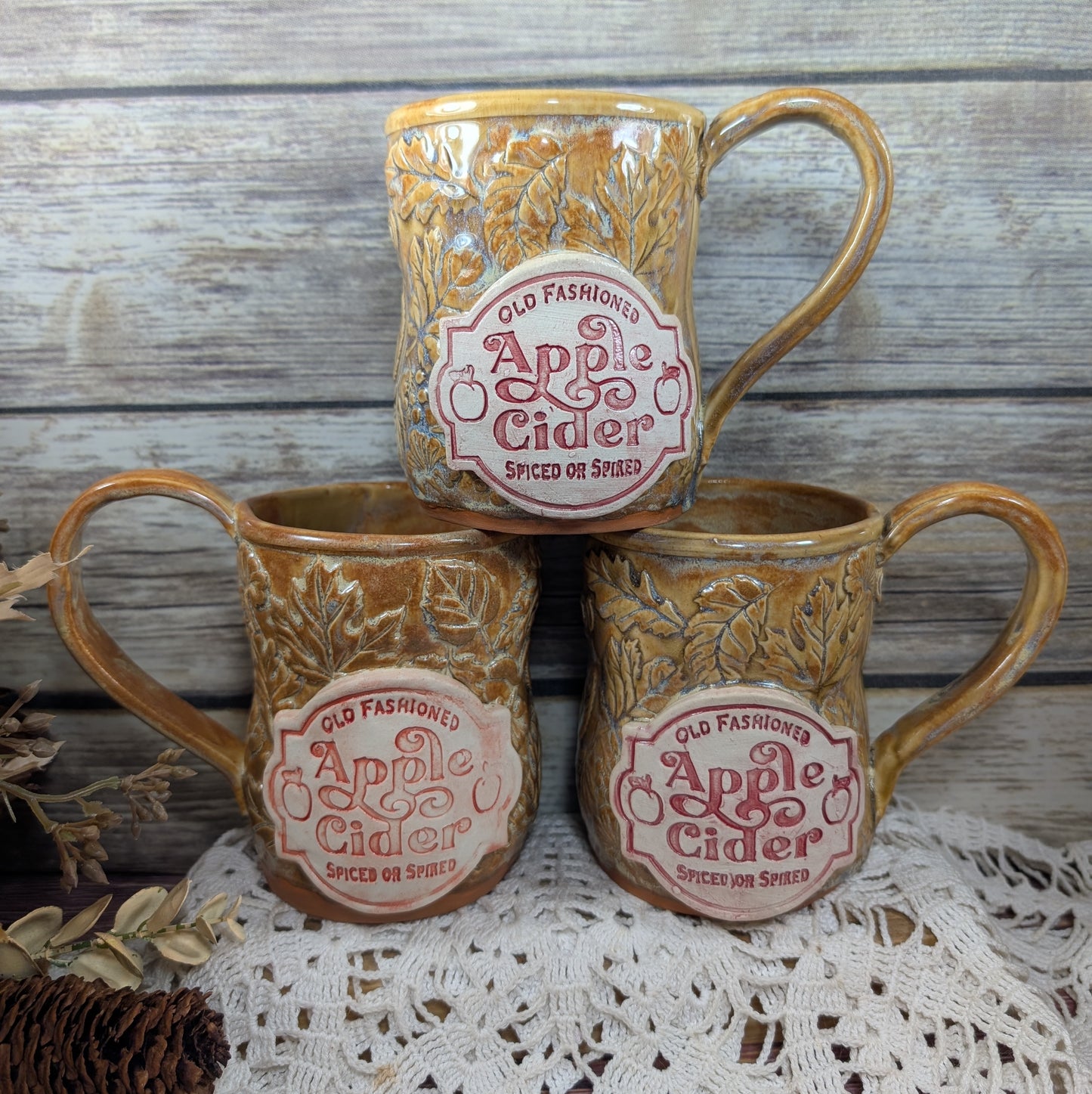 Three ceramic mugs with 'Old Fashioned Apple Cider' label on a wooden surface.