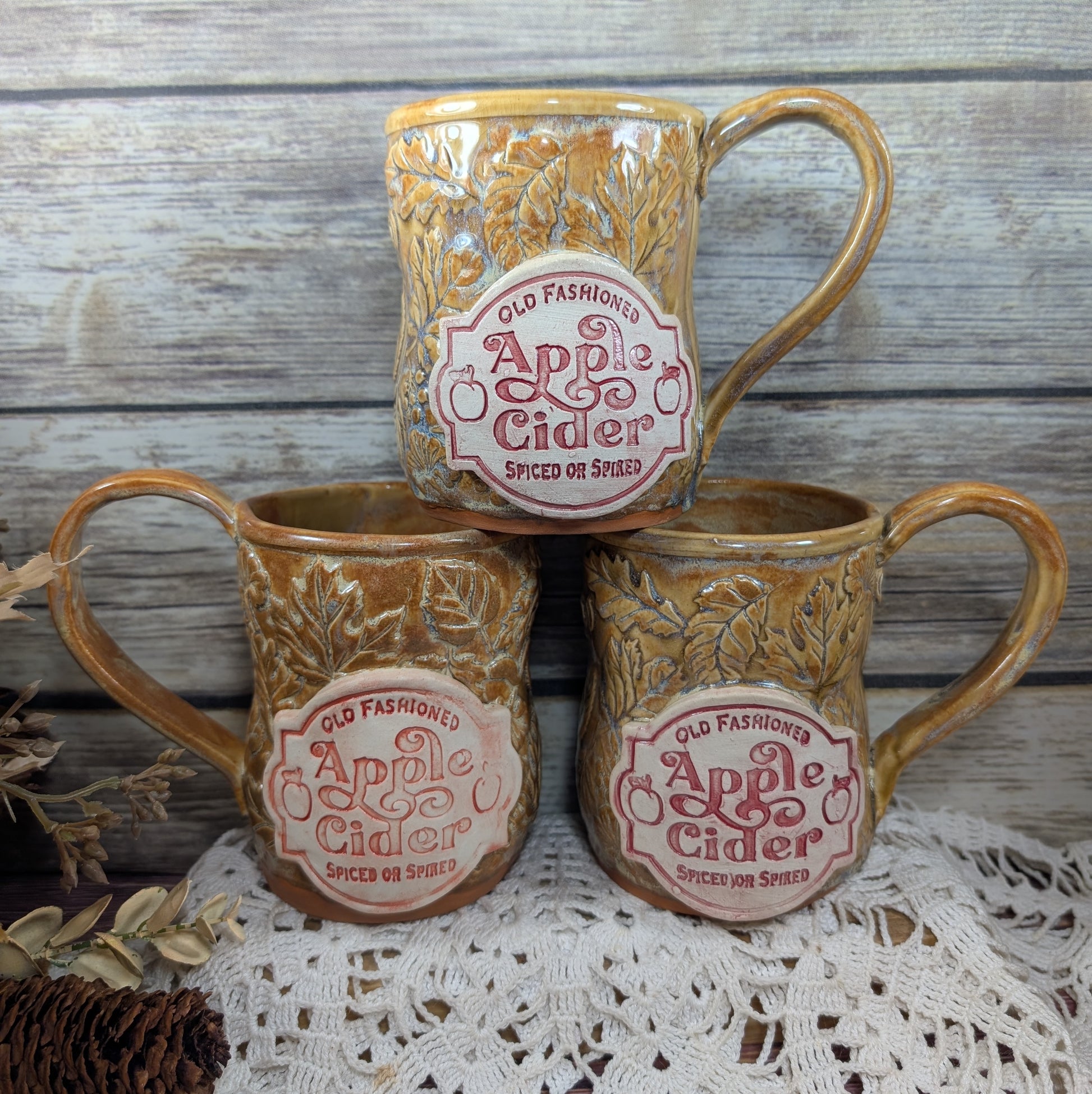 Three ceramic mugs with 'Old Fashioned Apple Cider' label on a wooden surface.