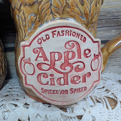 Decorative mug with 'Old Fashioned Apple Cider' label on a lace tablecloth.
