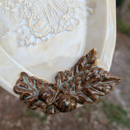 Decorative ceramic plate with leaf and acorn design on a blurred natural background