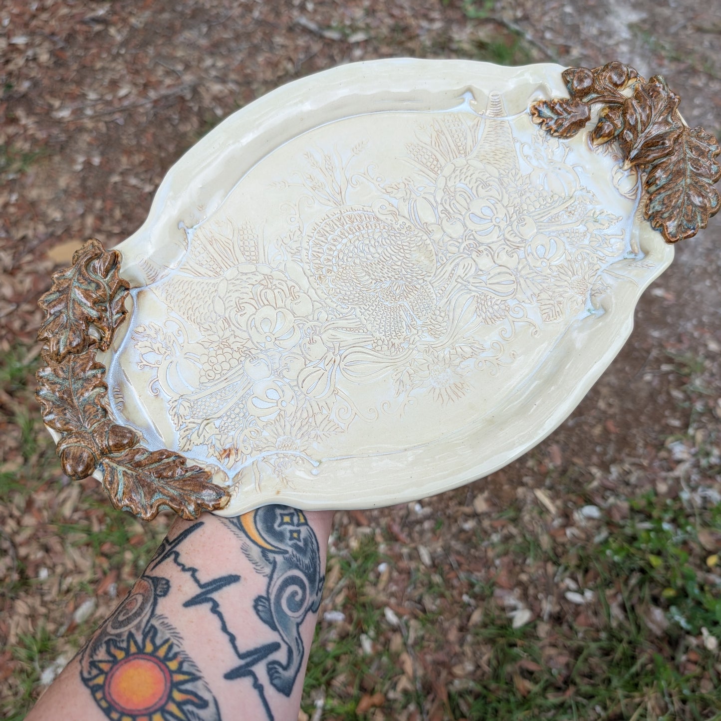 Decorative white tray with bronze leaf designs held by a person outdoors.