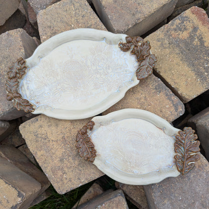 Two white ceramic oval trays with brown accents on a stone surface