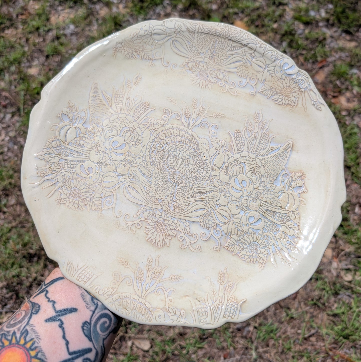 Decorative ceramic plate with floral patterns held by a person with tattoos outdoors.