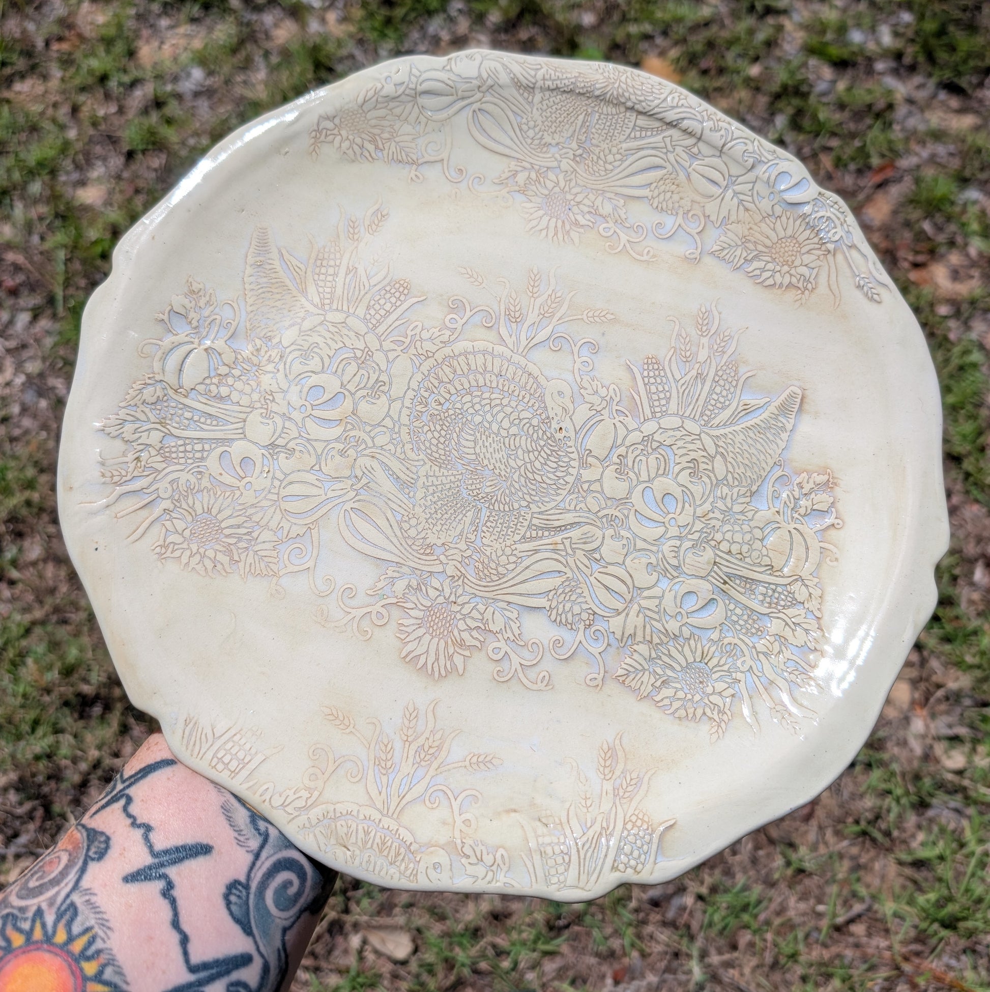 Decorative ceramic plate with floral patterns held by a person with tattoos outdoors.