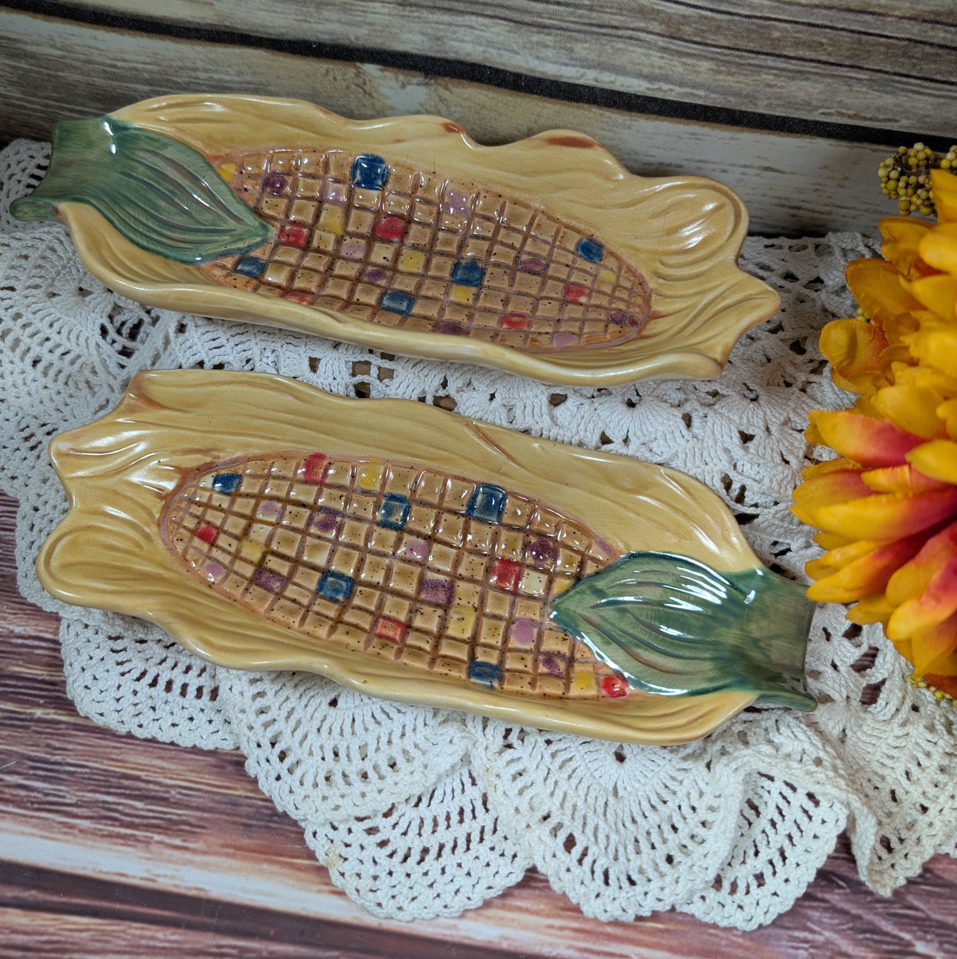 Two dishes the size, shape, and designed like an ear of corn on a lace doily on a wooden background. 