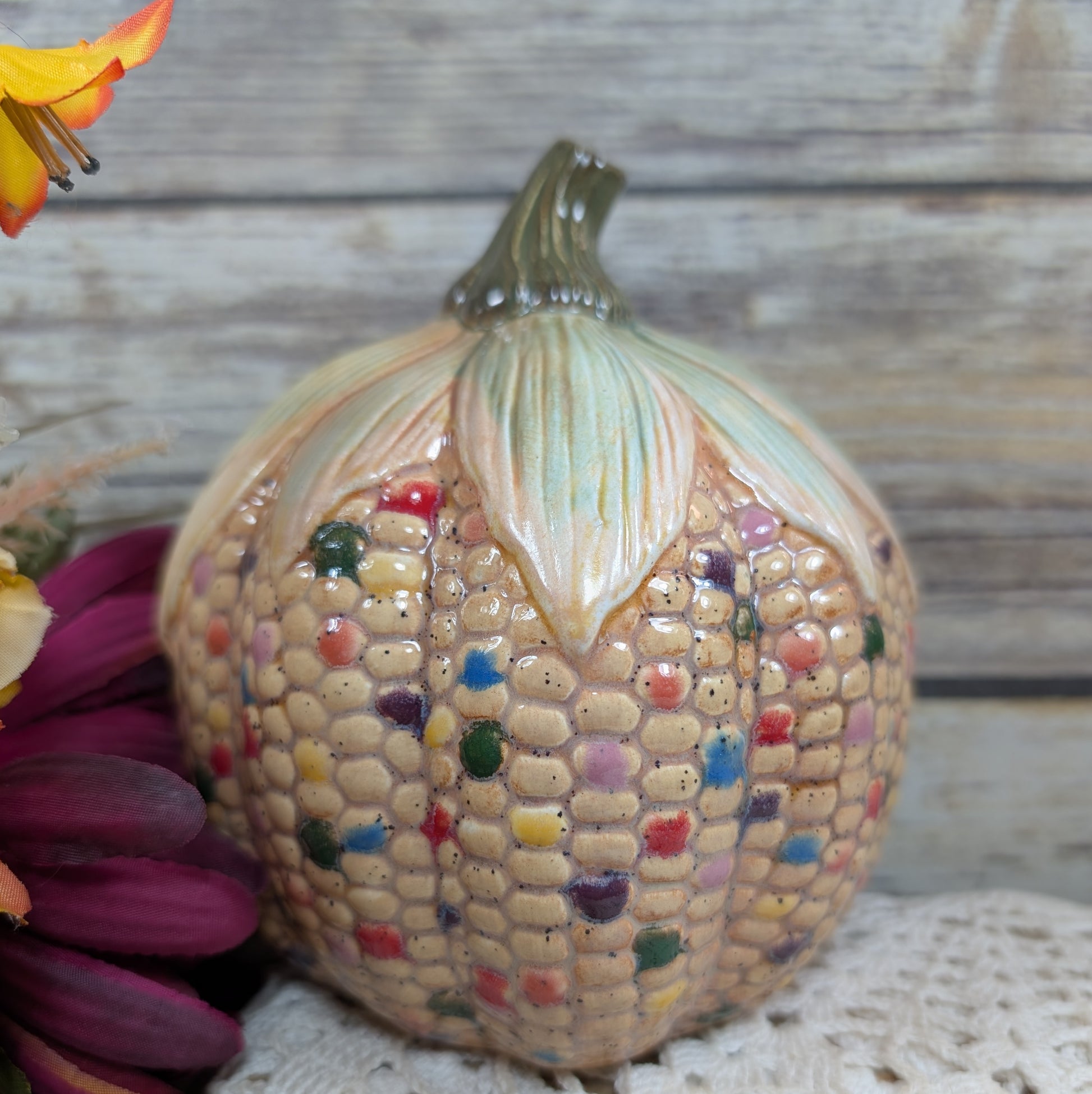 Decorative ceramic corn sculpture with colorful kernels on a wooden surface.