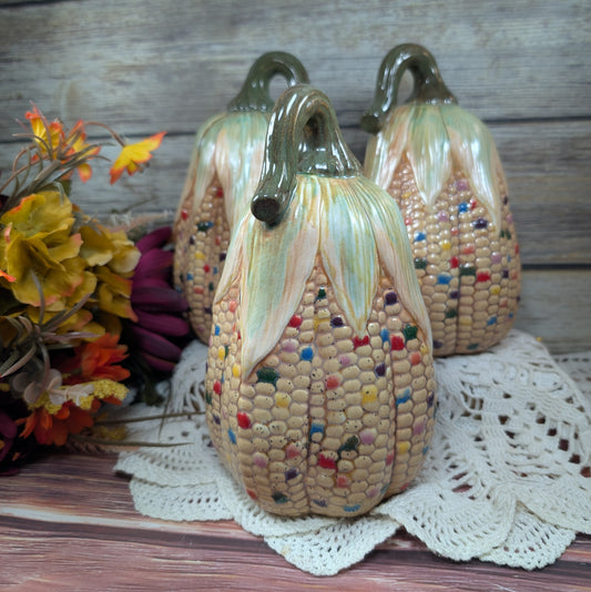 Decorative corn-shaped sculptures with colorful kernels on a wooden surface.