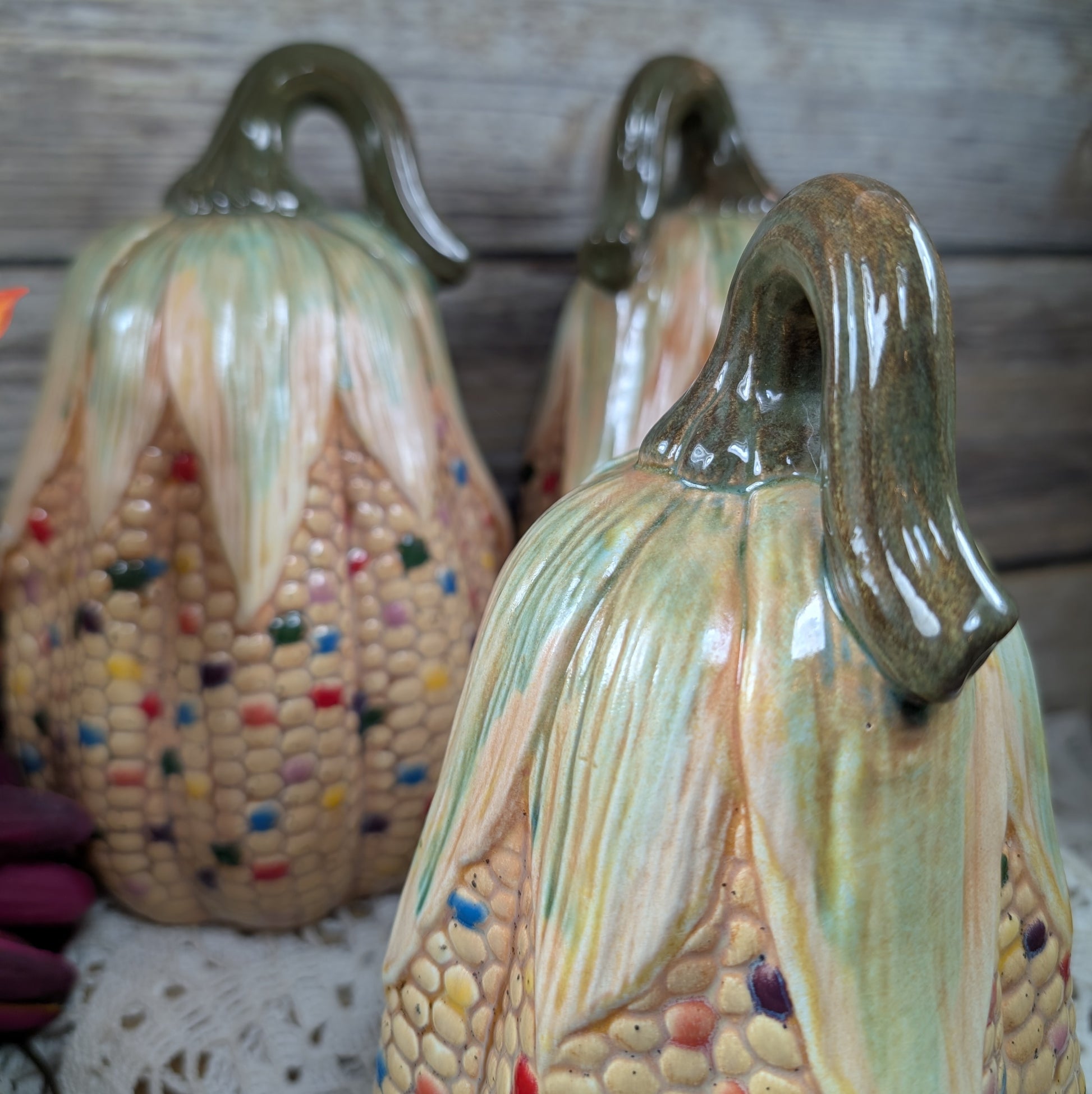 Three ceramic corn sculptures with colorful kernels on a wooden surface.