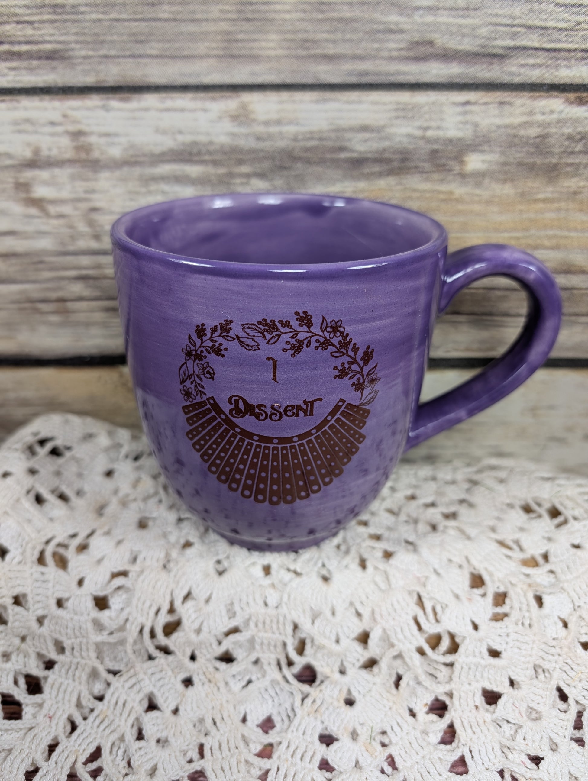 Purple mug with decorative text on a lace doily and wooden surface