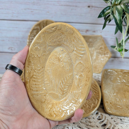 A hand holding a small oval dish. In back is the rest of the set of small ceramic trinket dishes, decorated with a mushroom motif, on a lace doily with a wooden background