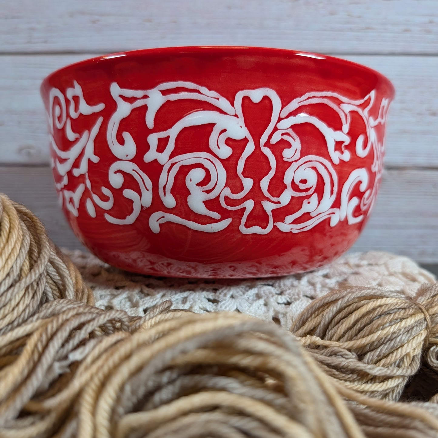 Red yarn bowl with white patterns on a wooden surface with yarn.