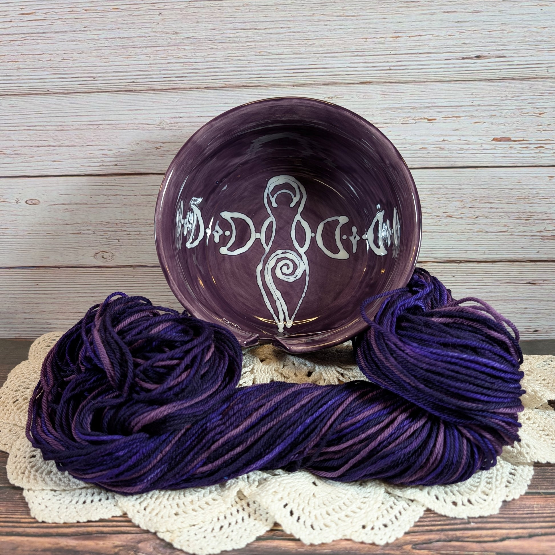Purple yarn skeins with a decorative purple yarn bowl on a wooden surface