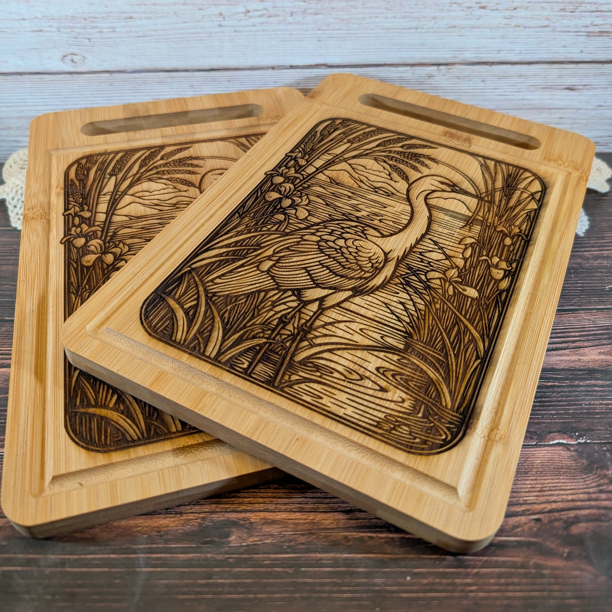 Two wooden charcuterie boards with engraved designs of a bird and nature on a wooden surface.