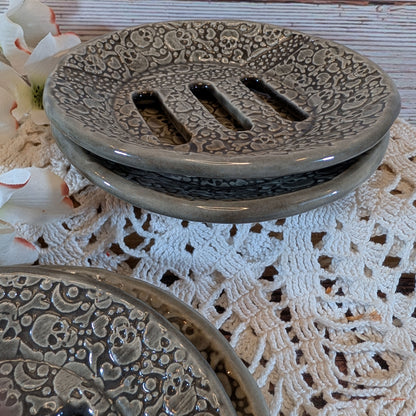 A set of round ceramic soap dishes with a raised floral pattern and three drainage slots, shown in a stacked arrangement on a white lace doily.
