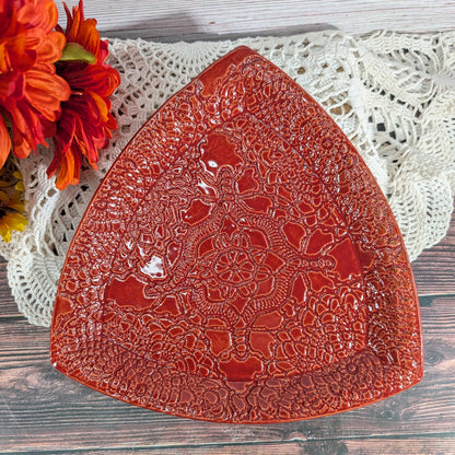 A red ceramic serving platter with an embossed floral pattern, styled on a white crochet doily with orange flowers in the corner.